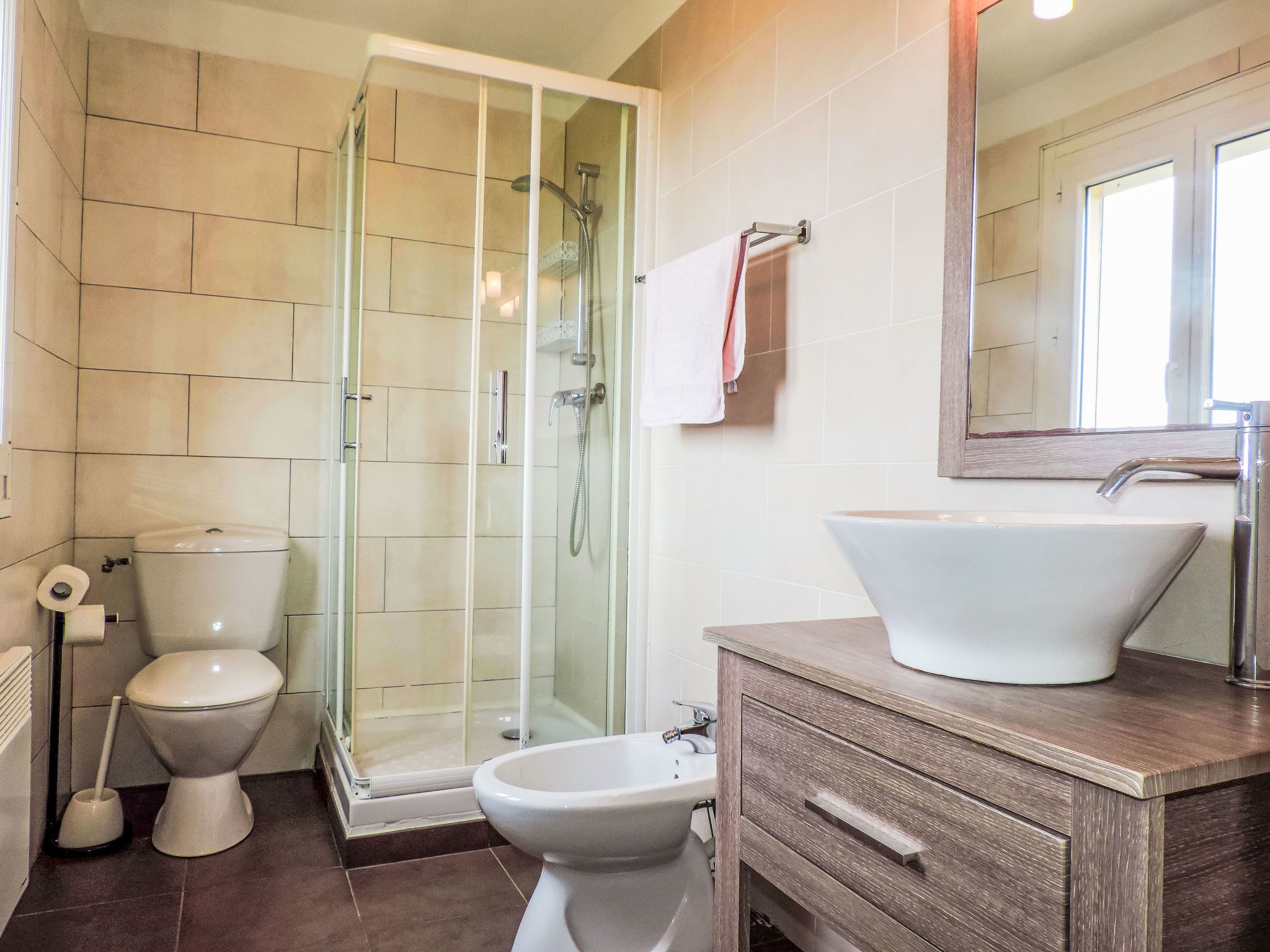 Un baño con ducha de vidrio, inodoro, bidé y lavamanos con un espejo grande arriba.