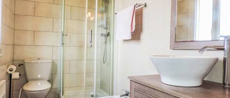 Un baño con ducha de vidrio, inodoro, bidé y lavamanos con un espejo grande arriba.