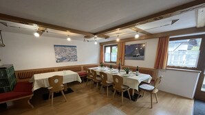Un comedor con mesas y sillas de madera, un banco rojo, y vistas al exterior a través de ventanas.