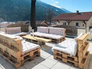 Outdoor seating with cushions on wooden pallets, a wooden table, and a view of mountains and houses in the background. - Zentral by Interhome (Pettneu am Arlberg)