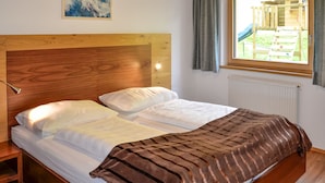Een slaapkamer met een houten hoofdbord, wit beddengoed en uitzicht op een speelruimte door een raam.