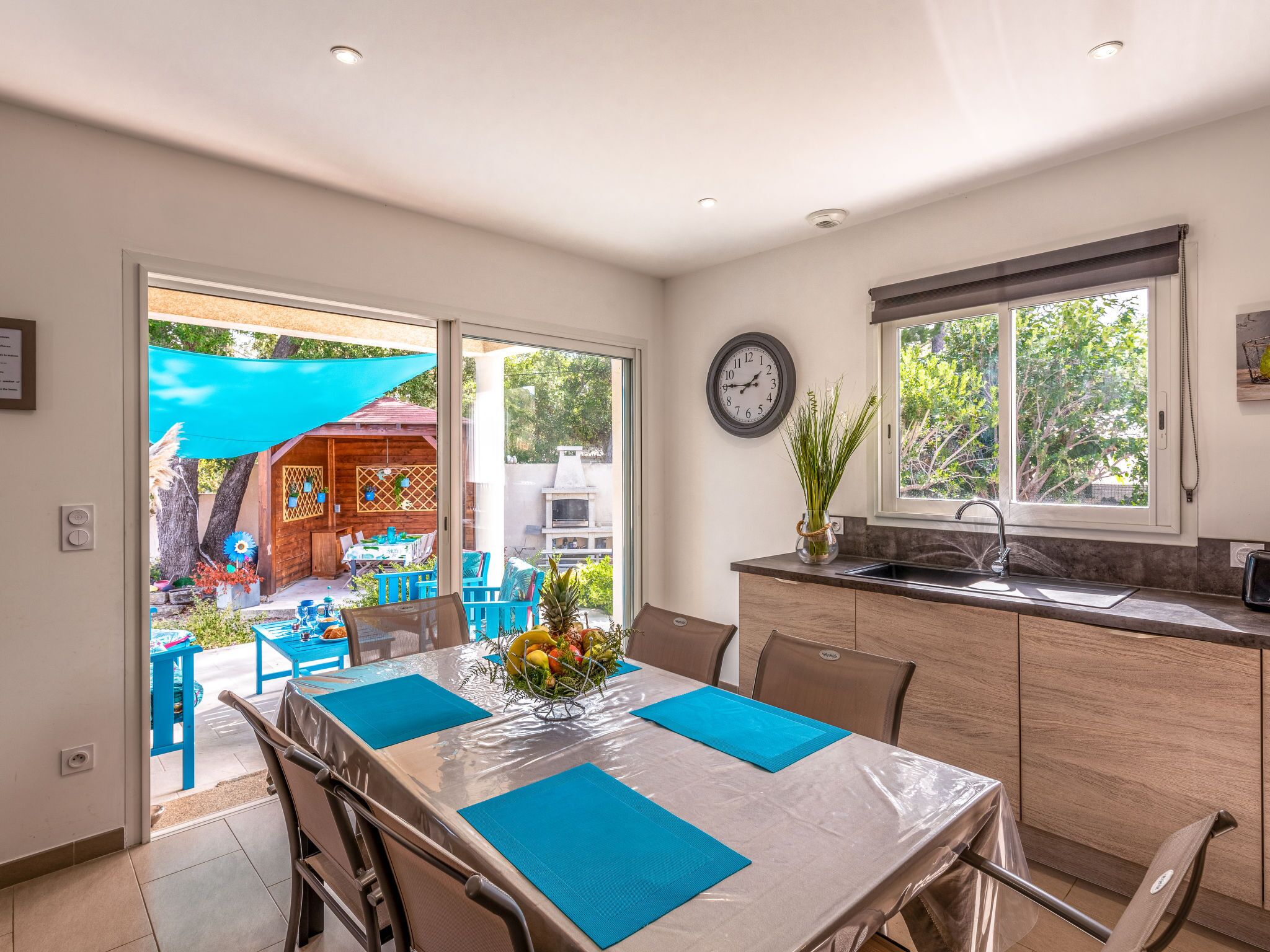 A modern kitchen with a dining area, large windows, and a view of the backyard.