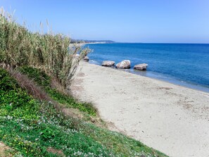 A beach with clear blue water, sandy shore, and some rocks.