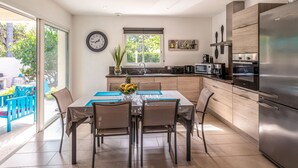 A modern kitchen with a dining area, featuring a stainless steel refrigerator, microwave, and oven, a large window, and a dining table with chairs. - Villa Marie-Jo by Interhome (Prunete)