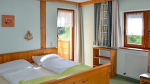 A wooden bed with a green blanket, a wooden nightstand, a window with curtains, and a view of greenery outside.