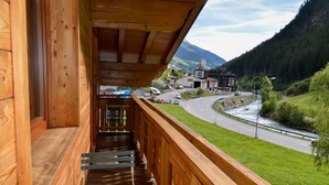 A wooden balcony with a view of a winding road and a river, overlooking a town and mountains.