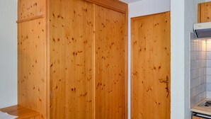 A wooden wardrobe in a bathroom with a tiled wall and a small sink.