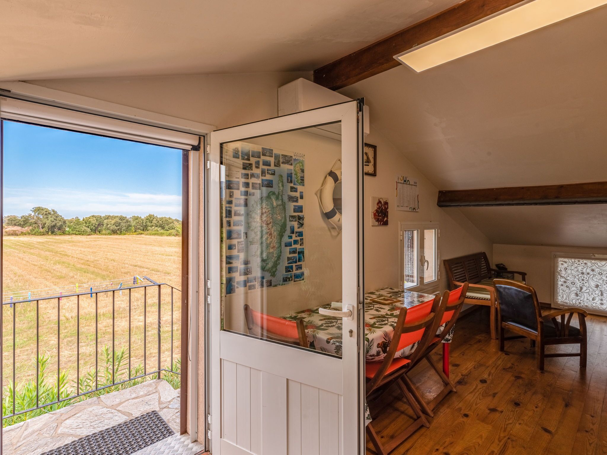 A dining area with a table and chairs, a view of a field through a glass door, and a wall with a map.