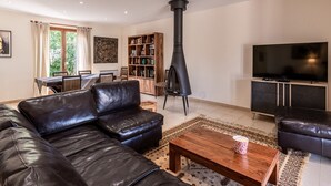 Un salon moderne avec un canapé en cuir noir, une table basse en bois, un téléviseur, une bibliothèque et une cheminée.