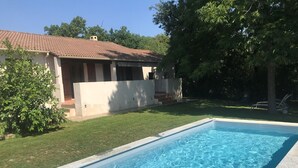 Une piscine rectangulaire à l’eau d’un bleu limpide, entourée d’une pelouse bien entretenue et d’une maison dont le toit est recouvert de tuiles.