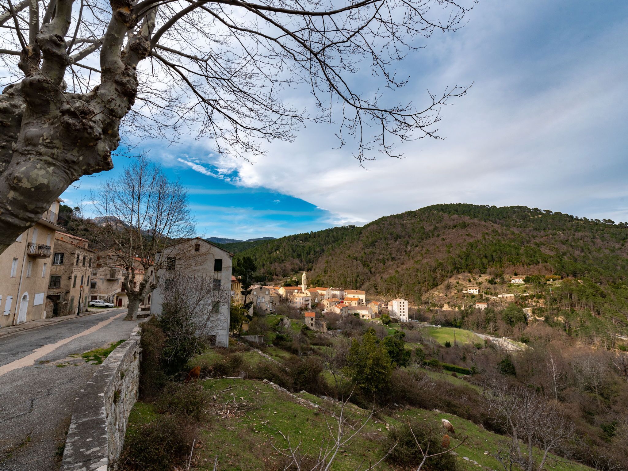A rural village with traditional stone buildings, a church, and a hill in the background.