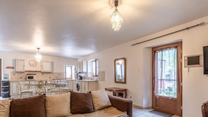 Una sala de estar con un sofá, una mesa de centro de vidrio, un comedor con sillas, una cocina con microondas y una puerta de madera.