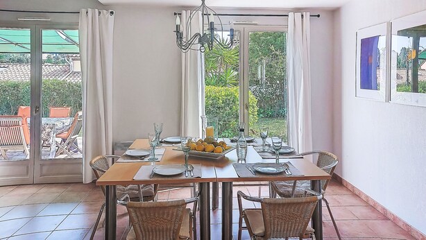 A dining area with a table set for four, large windows with curtains, and a view of greenery outside. - Olivier by Interhome (Mougins)
