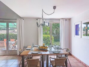 Zona pranzo con tavolo apparecchiato per quattro persone, ampie finestre con tende e vista sul verde.
