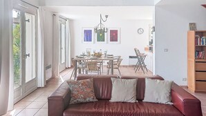 A spacious living area with a leather sofa, dining table, and chairs. There is a staircase leading to an upper level, and artwork is displayed on the walls. - Olivier by Interhome (Mougins)