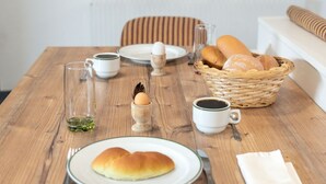 Una mesa de comedor con un plato de pan, una taza de café y una cesta de bollos.