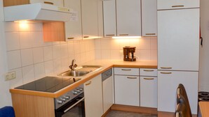 Une cuisine compacte avec des meubles blancs, une cuisinière, un four, un évier et une machine à café.