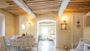 A dining area with a table set for two, a sofa, and a chair in a room with a tiled floor and wooden ceiling beams. - Le Clermont by Interhome (Chateauneuf de Grasse)