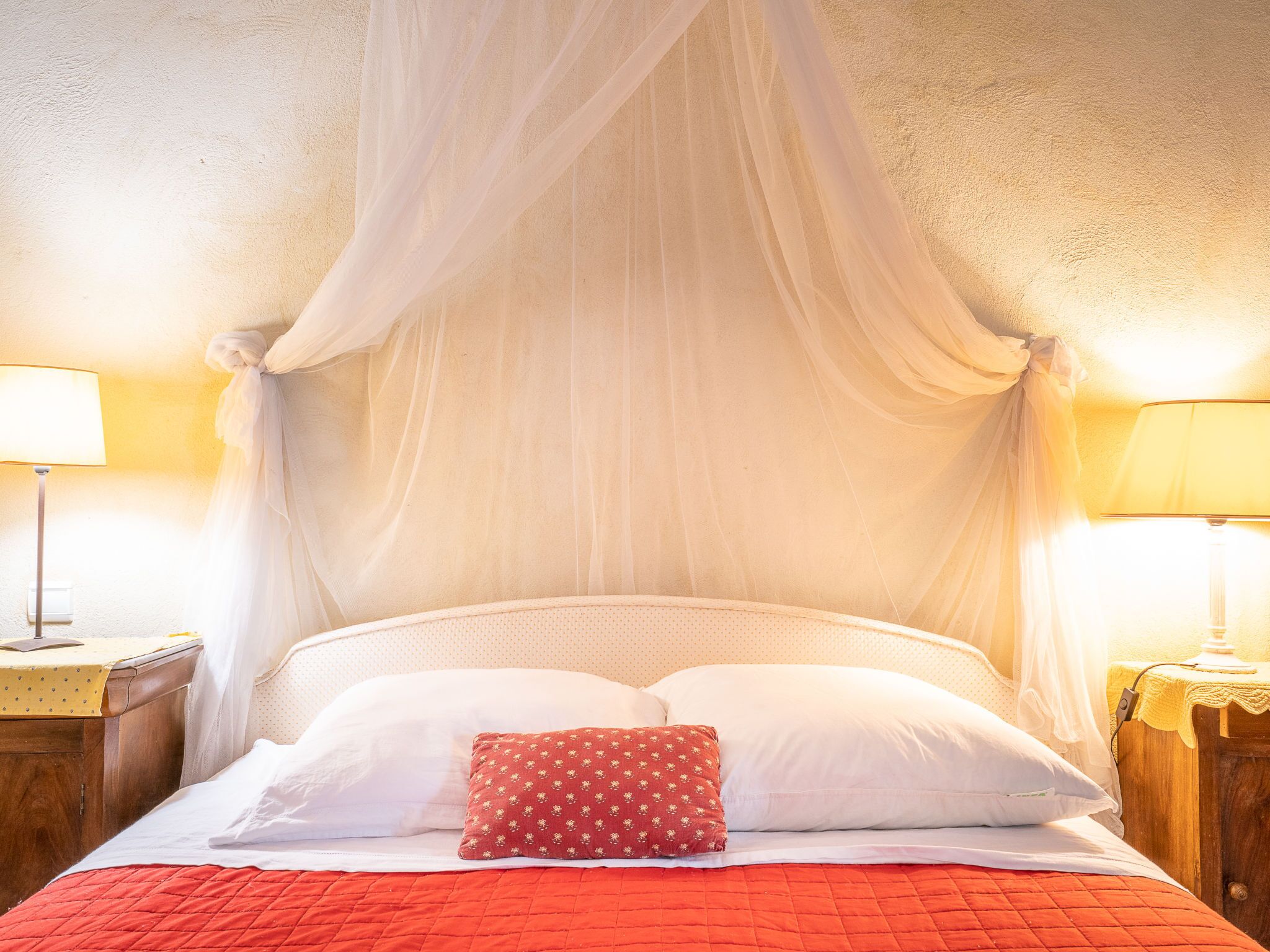 Ein Bett mit weißen Leinentüchern, einer roten gesteppten Bettdecke und einem roten Kissen mit einem Blumenmuster.