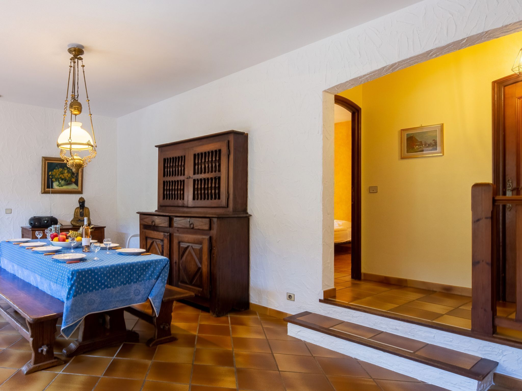 A dining area with a table set for four, a wooden cabinet, a Buddha statue, and a chandelier.
