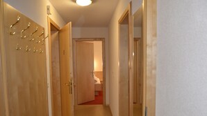Un couloir avec des portes en bois, un sol recouvert de moquette et une salle de bain visible, équipée d’un lavabo et d’un miroir.