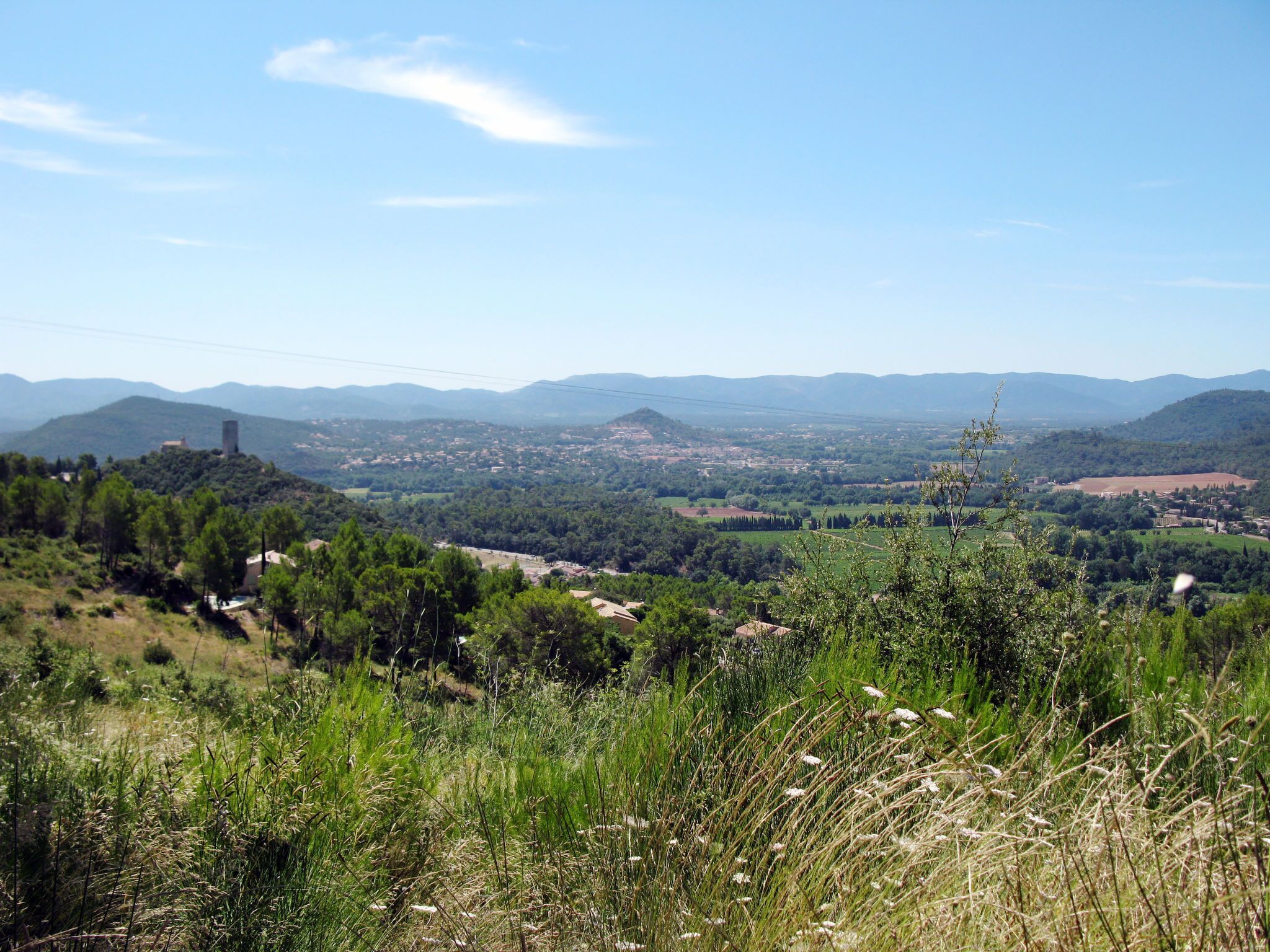 Vista panorámica de un pueblo con una torre destacada en una colina, rodeado de vegetación exuberante y montañas lejanas.