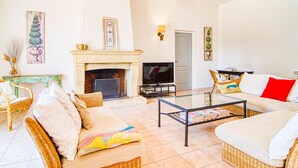 Sala de estar com lareira, televisão, móveis de vime e uma porta que dá para outro cômodo.
