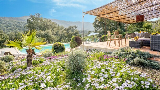 Ein Poolbereich mit einer Pergola, Sitzgelegenheiten im Freien und Blick auf die Berge.