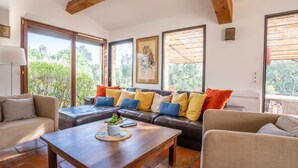 Ein geräumiges Wohnzimmer mit einer Ledersofa, einem Holztisch und Blick ins Grüne durch große Fenster.