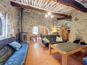 A stone-walled room with a fireplace, leather sofa, wooden table, and a cozy seating area.