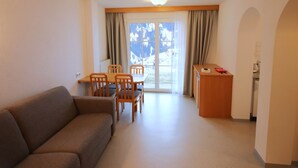 Una sala de estar con un sofá, una mesa de comedor con sillas, una zona de cocina y vistas a montañas a través de un ventanal.