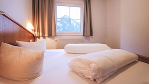 Quarto de hotel com duas camas, uma janela e vista para as montanhas, e cabeceira de madeira.