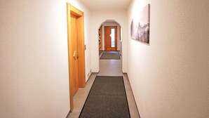 Um corredor com porta de madeira, tapete na entrada e um quadro na parede.