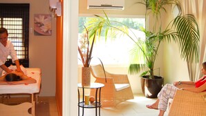 A massage therapy room with a massage table, a wicker chair, and a potted plant.