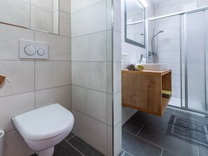 A modern bathroom with a toilet, a wooden vanity, a shower, and a mirror. - Martina by Interhome (Kappl)