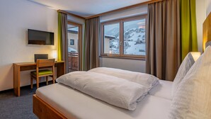 A hotel room with a bed, a desk, a chair, a television, and a window with a view of a snowy landscape.