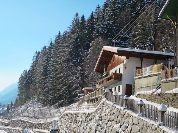 A snow-covered mountain road with a wooden house on a stone wall, surrounded by evergreen trees. - Hedwig Jäger by Interhome (Kappl)