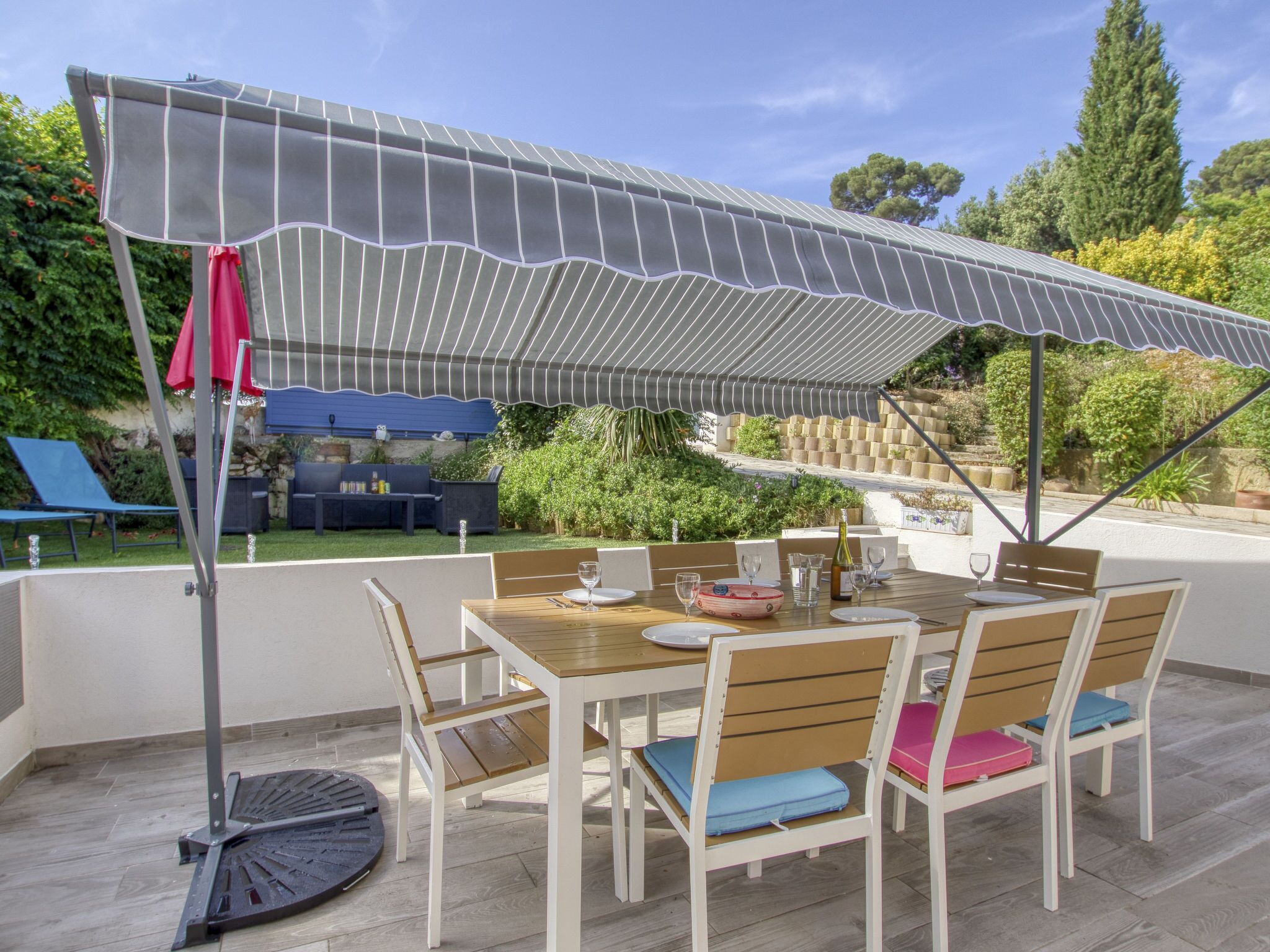 Una terrazza esterna con un tavolo apparecchiato per mangiare, circondata da sedie con cuscini.