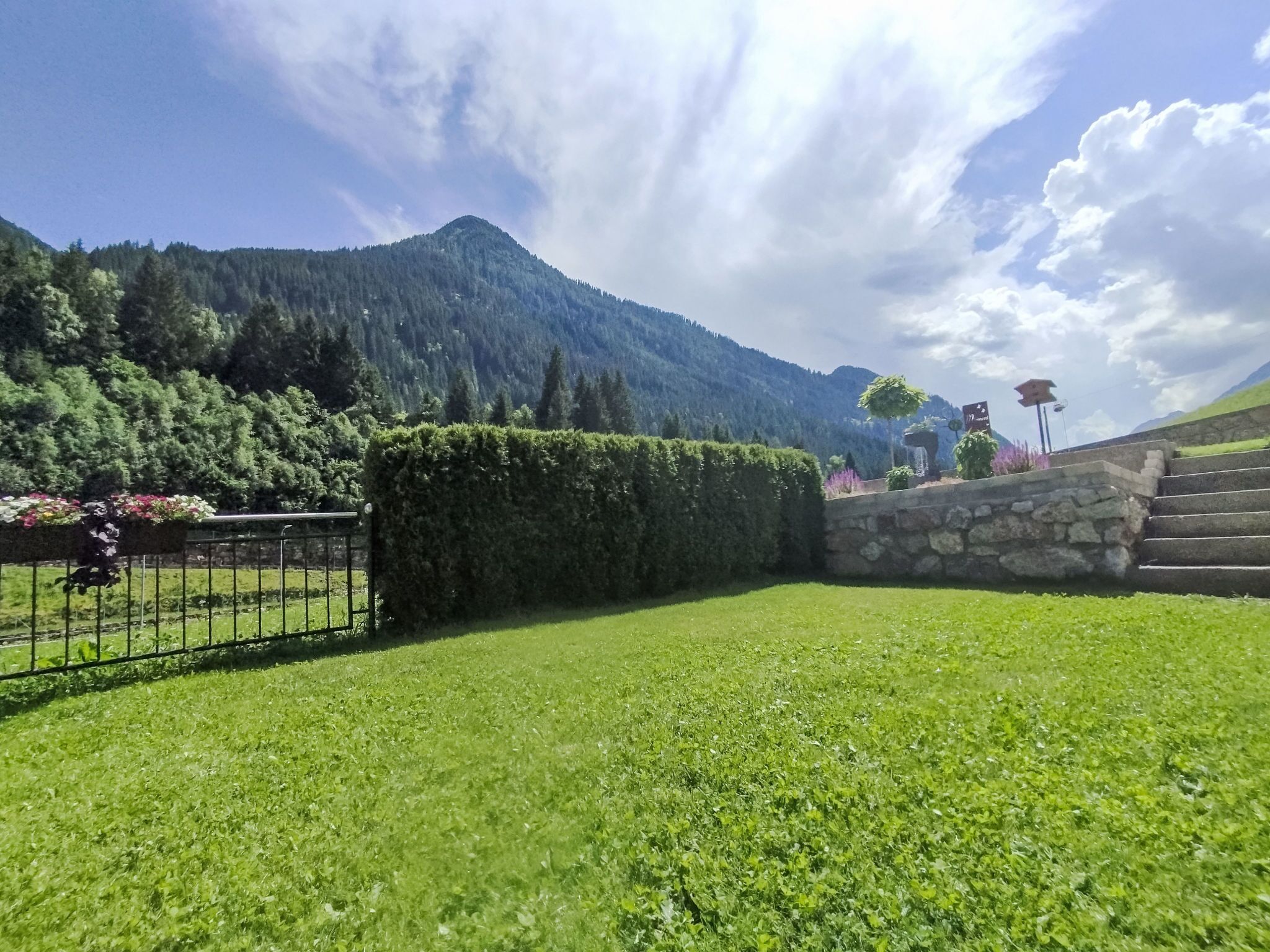 A well-maintained lawn with a stone wall and steps leading up to a mountain.