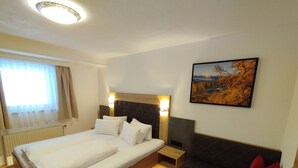 Ein Hotelzimmer mit einem großen Bett, Holzboden, einer dunklen Couch mit rotem Kissen, einem Wandbild und einem Fenster mit Vorhängen.