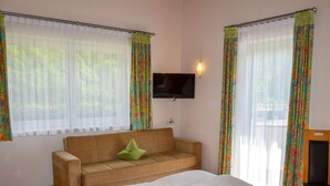 A hotel room with a bed, a sofa, a TV mounted on the wall, and curtains. - Apart Garni Wachter by Interhome (Kappl)