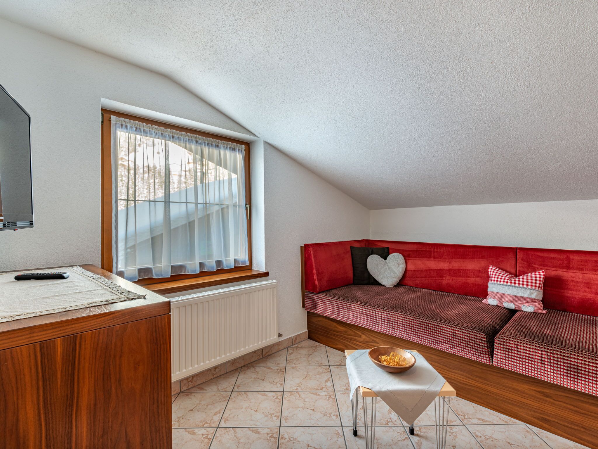 A cozy room with a red sofa, a small table with a bowl, a window with curtains, and a radiator.