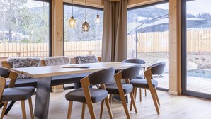 A modern dining area with a wooden table and chairs, large windows, and a view of a wooden deck and mountains. - #7b mit Sauna & Pool by Interhome (Sankt Georgen am Kreischberg)