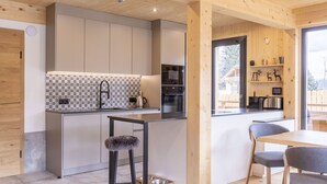 A modern kitchen with a central island, bar stools, and a dining area with wooden chairs. - #7b mit Sauna & Pool by Interhome (Sankt Georgen am Kreischberg)