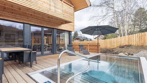 An outdoor swimming pool area with a wooden deck, a glass-enclosed patio, and a view of the surrounding landscape. - #7b mit Sauna & Pool by Interhome (Sankt Georgen am Kreischberg)