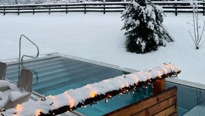 Ein verschneiter Außenbereich mit Pool, Holzterrasse und Blick auf eine verschneite Landschaft.