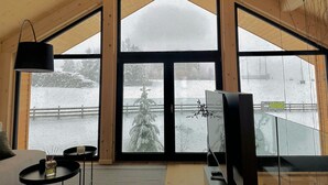 Ein Zimmer mit großen Fenstern, einem Bett, einem Fernseher und einem kleinen Tisch mit einer Vase und einer Kerze.