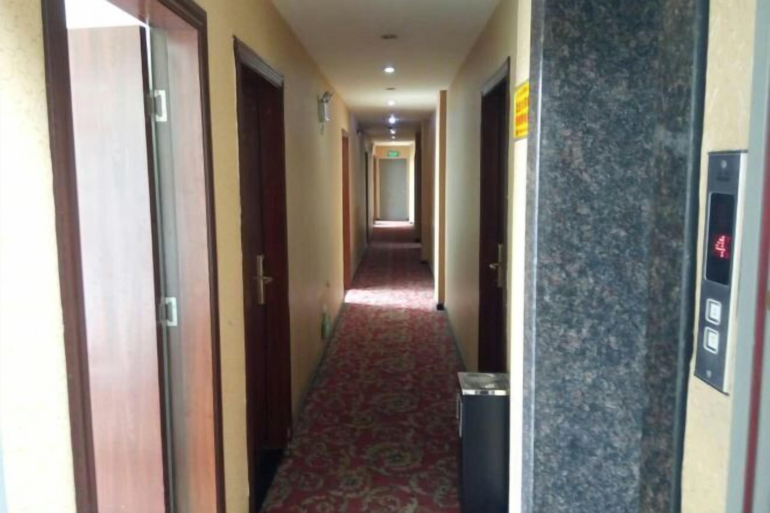 A hotel corridor with a carpeted floor, doors on the left, and an elevator on the right.