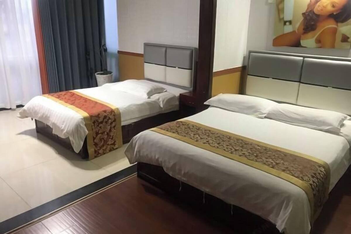 Habitación de hotel con dos camas individuales, suelo de madera, un espejo grande y un cuadro en la pared.