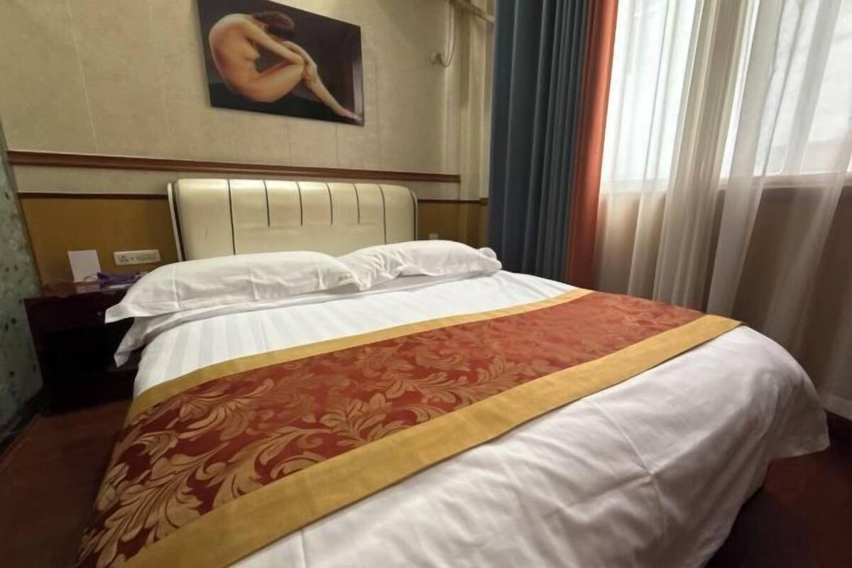Habitación de hotel con cama, mesita de noche, un cuadro en la pared y una ventana con cortinas.